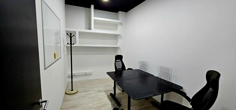 Compact private office at Rua Santo Adrião, Braga featuring a black desk, two chairs, and white shelving.