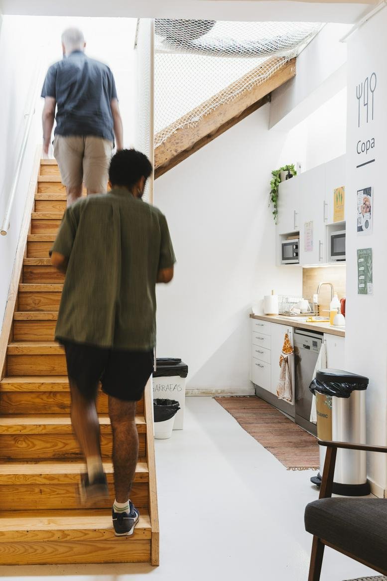 Wide-angle interior of Rua Saraiva de Carvalho 1C Lisbon showing a bright kitchen and wooden staircase.