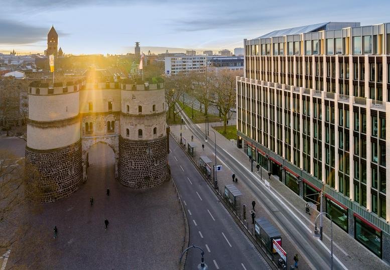 Exterior of the modern office building at Rudolfplatz 3, Cologne, overlooking the historic Hahnentor gate.