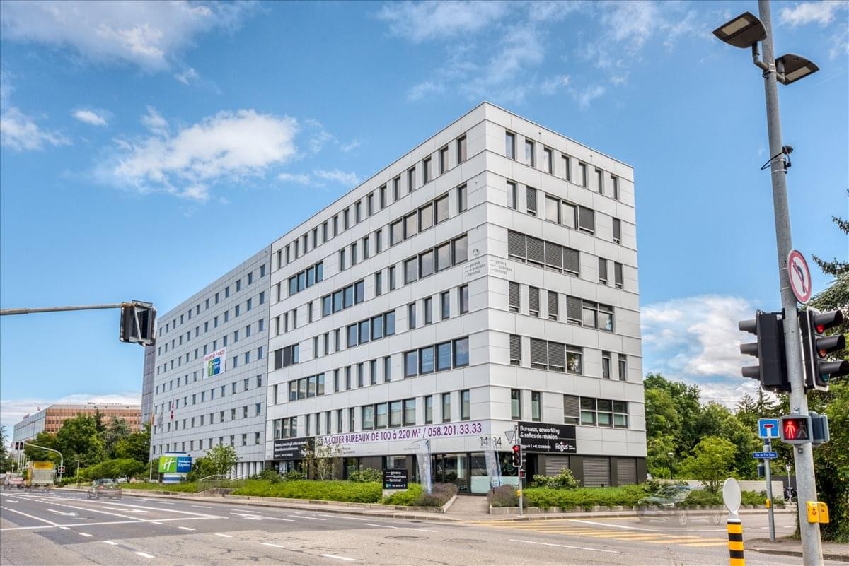 Exterior view of the modern white office building at Rue de Pré-Bois 14, Meyrin.