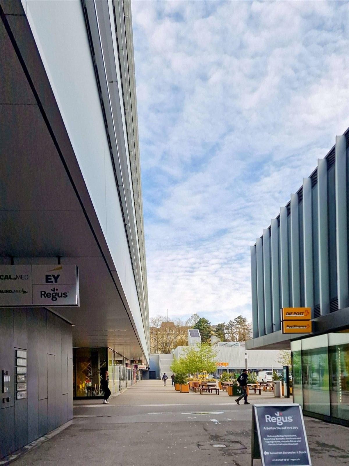 Wide view of a public walkway between modern commercial buildings and retail storefronts.