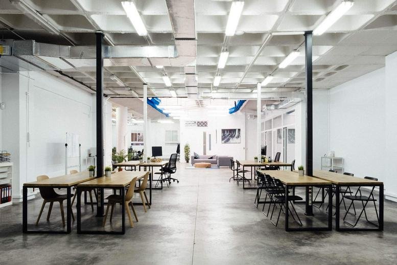 Spacious open-plan workspace at Sevilla, Seville, Spain with wooden desks and industrial lighting.