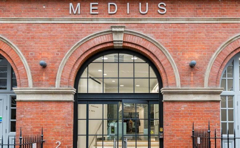 Brick exterior of the Medius building at Sheraton Street, London featuring an arched glass entrance.