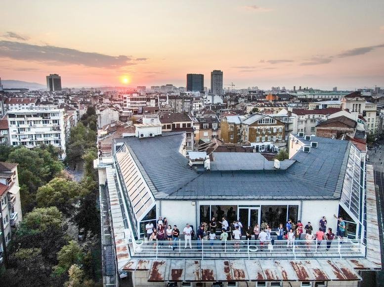 Rooftop view of the Sofia Center building at sunset with a terrace full of people.