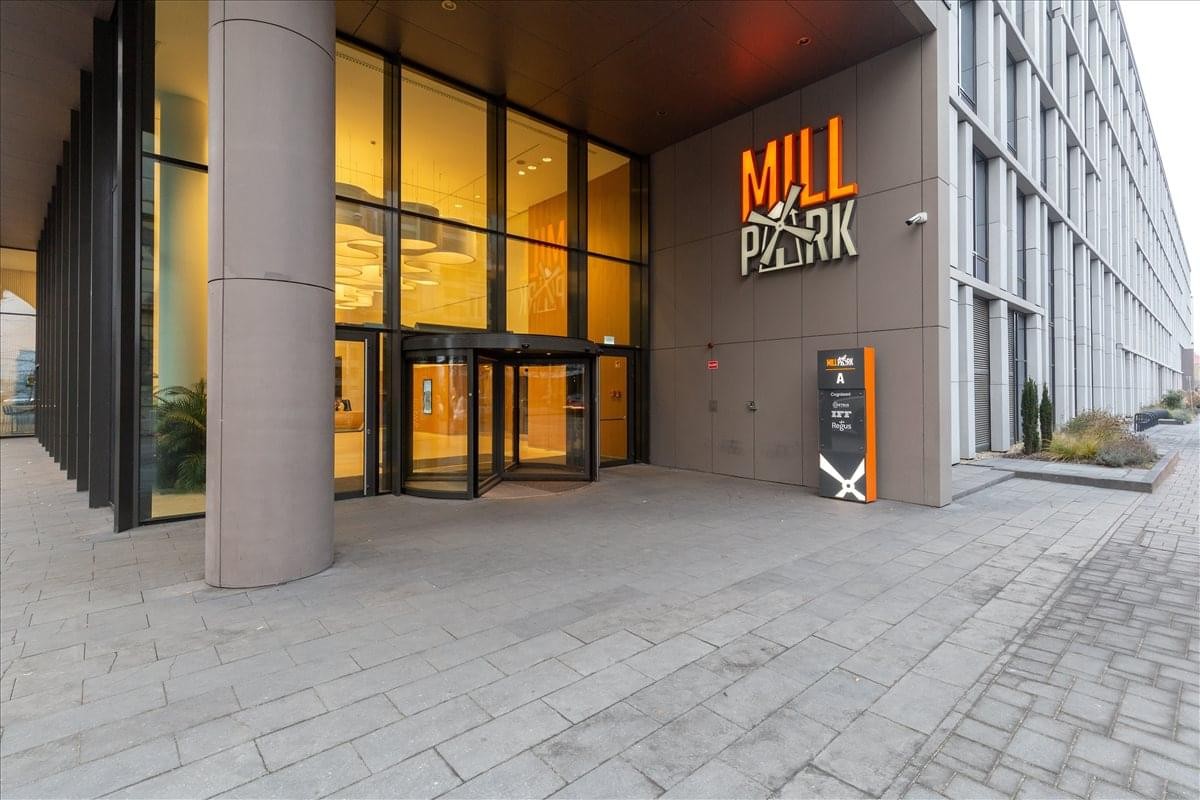 Exterior entrance of Mill Park building with glass revolving doors and modern signage.
