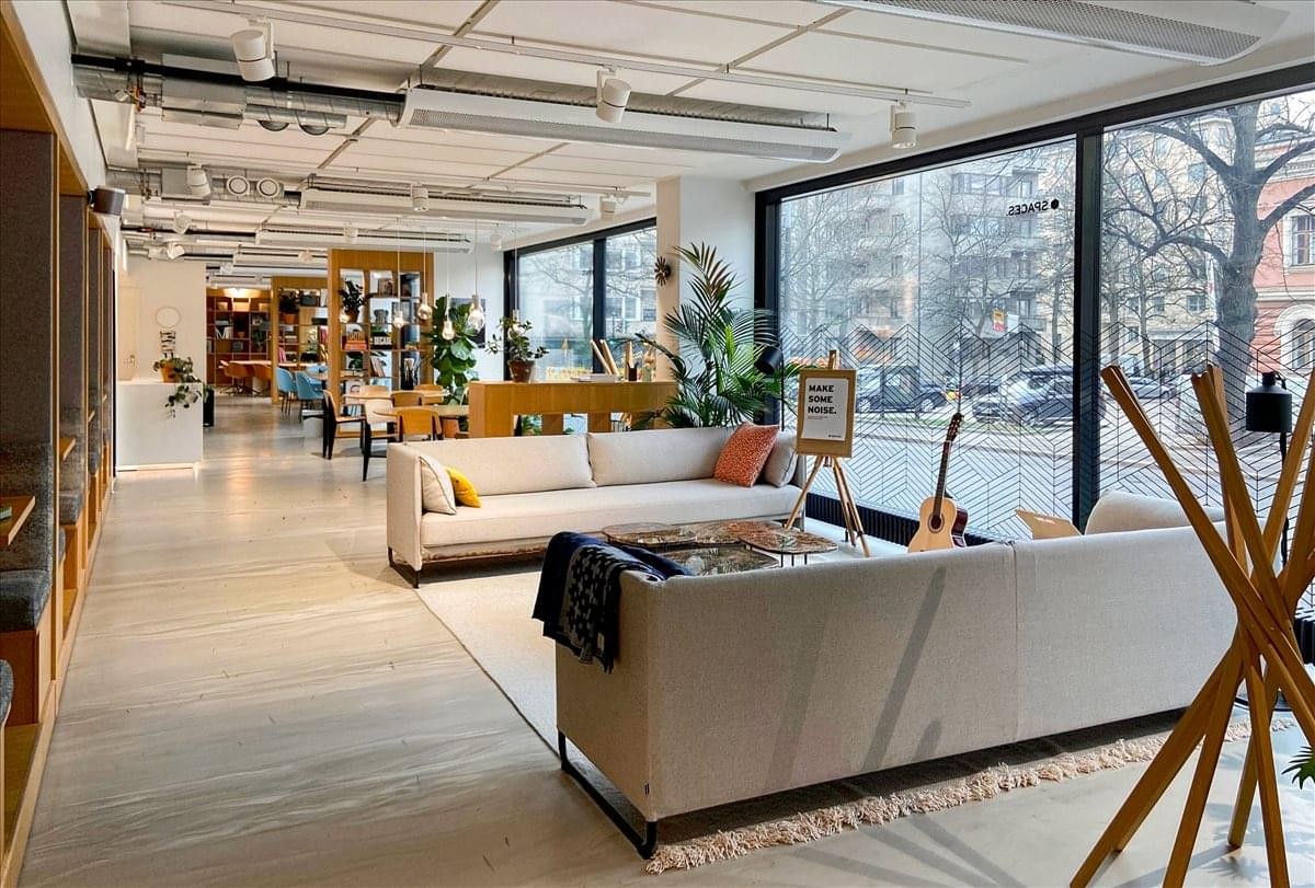 Spacious lounge area at Spaces Bulevardi featuring white sofas, wooden floors, and large windows with street views.