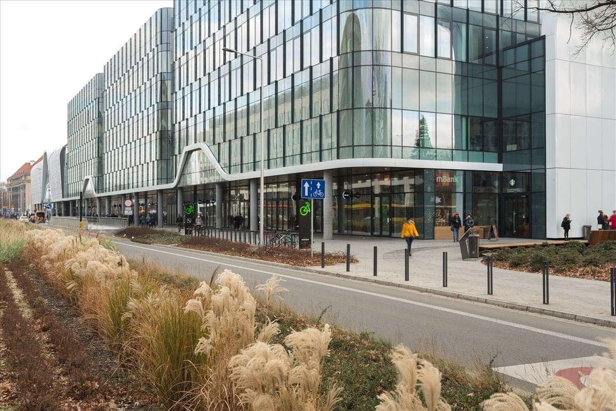 Modern glass-facade exterior of the Spaces Wroclavia building on a bright day.