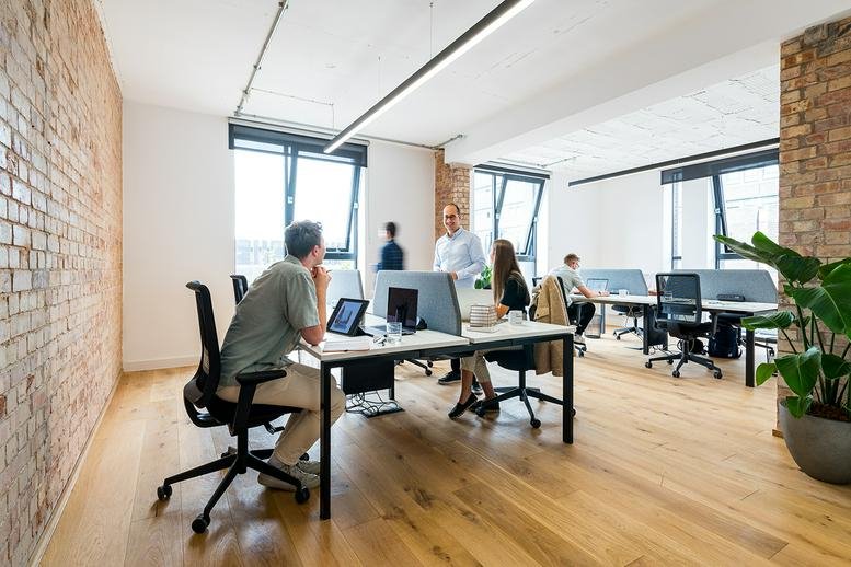 Spacious open-plan office with exposed brick walls, wooden floors, and natural light.