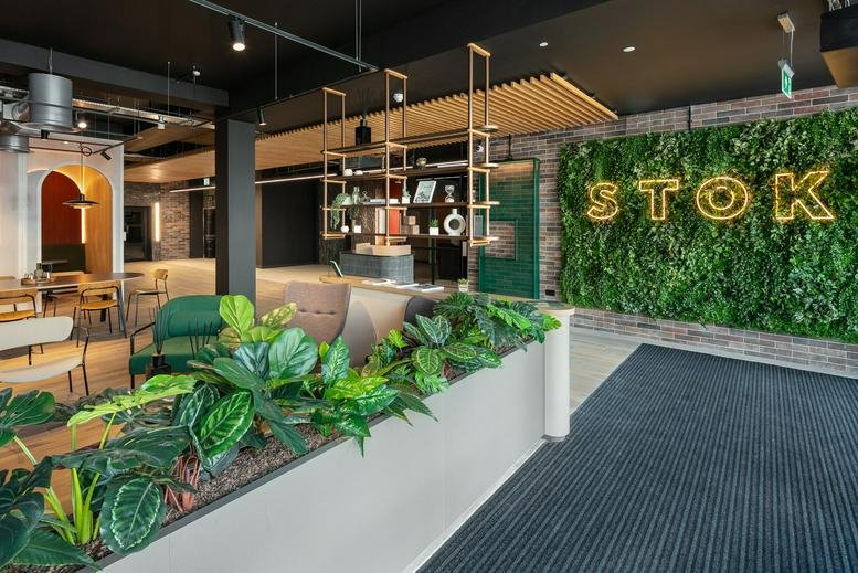 Lounge area at STOK with green armchairs and a vibrant plant-covered feature wall with neon signage.