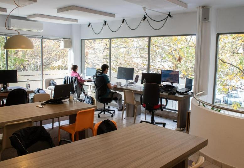 Spacious open-plan office at Street Napoleontos Zerva 10 featuring desks and large windows overlooking trees.