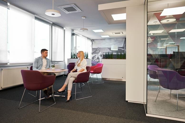 Lounge area with colorful armchairs and natural light from large windows.