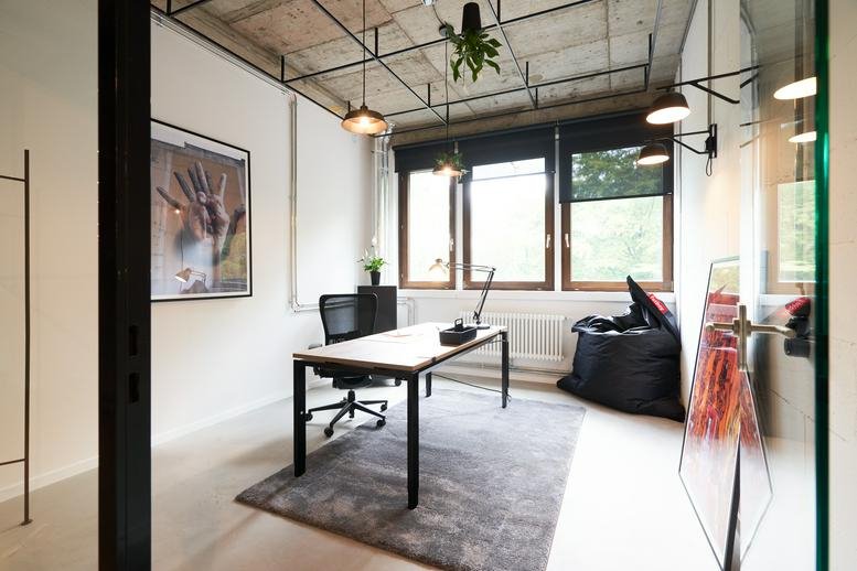 Spacious private office with a wooden desk, grey rug, and industrial ceiling details.