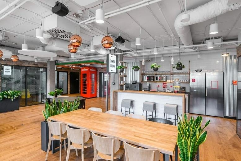 Spacious coworking lounge at Tadeusza Czackiego 15/17 with a wooden table, hanging plants, and a red phone booth.