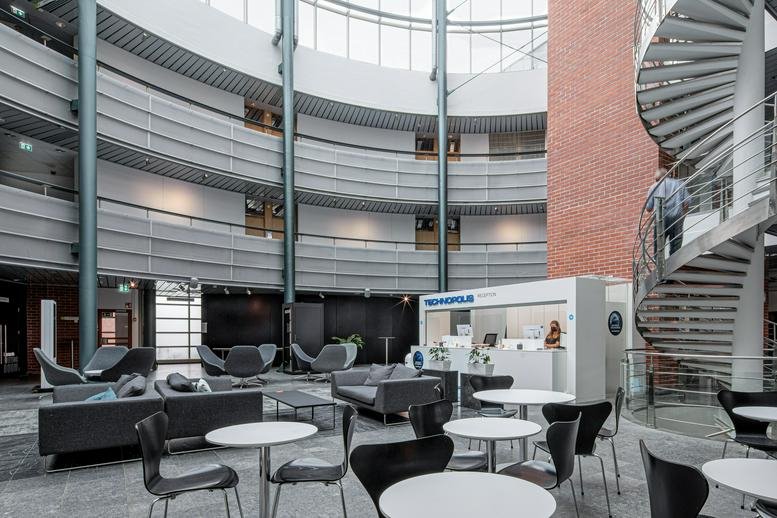 Spacious circular atrium at Tekniikantie 12 with a spiral staircase, lounge seating, and a service kiosk.