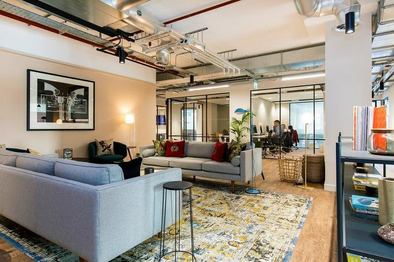 Spacious lounge area with gray sofas, a patterned rug, and industrial ceilings at Thames Tower.