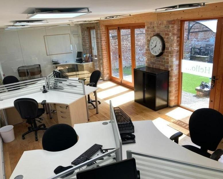Open-plan office area with white desks, black chairs, and natural light from large windows.