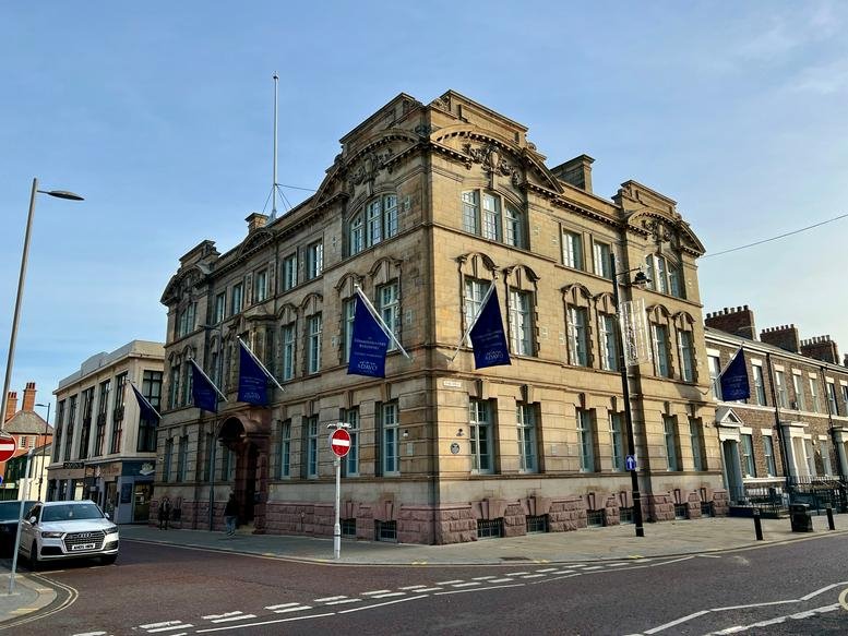 Grand stone exterior of The Commissioners Building featuring blue flags and arched windows.