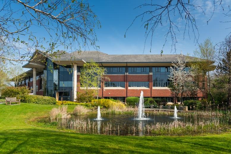 Exterior view of the brick and glass facade of The Lambourn overlooking a pond with fountains.