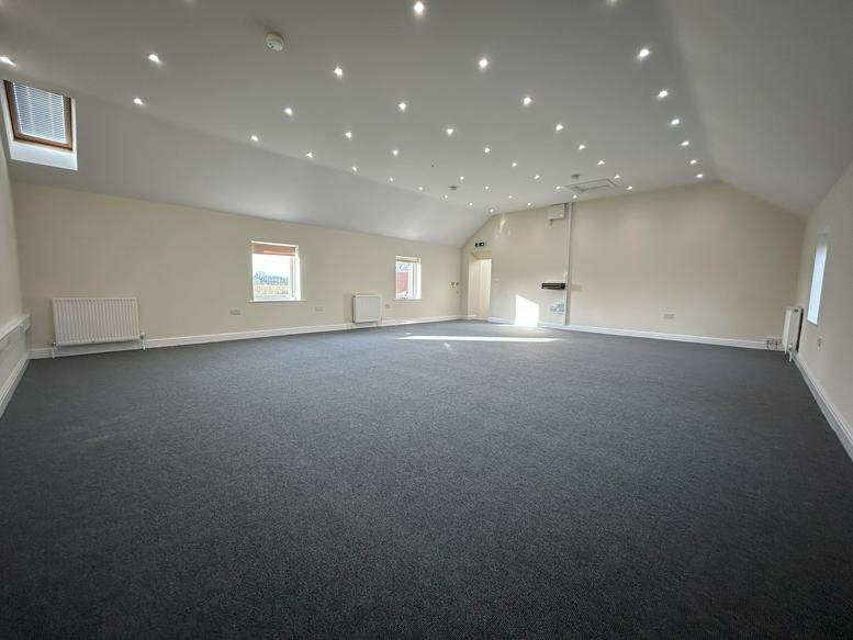 Spacious open-plan office with grey carpeting and numerous recessed ceiling lights.