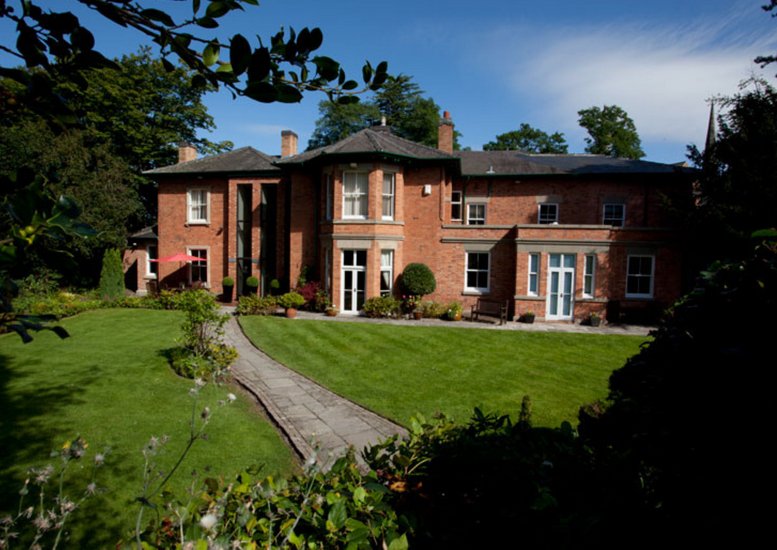 Wide view of the red brick exterior with a paved path leading through a well-maintained lawn.
