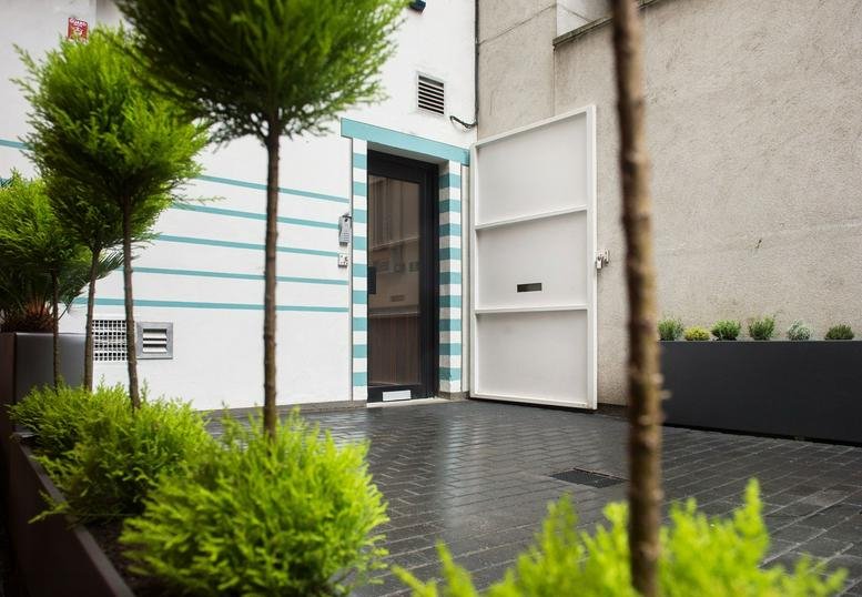 The entrance to The Sandwich, 10 Clothier Street, London, featuring striped wall details and manicured greenery.