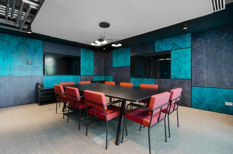 Spacious boardroom at The Shepherds Building featuring colorful teal wall panels and red chairs.