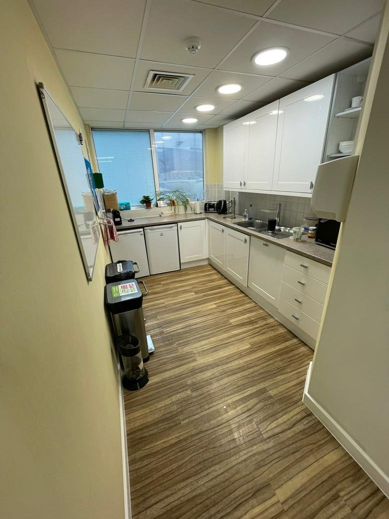 Modern communal kitchen at The Slade, Tonbridge, Kent with wood-style flooring and white cabinetry.