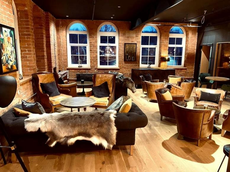 Spacious communal lounge at The Tannery featuring leather armchairs, arched windows, and a faux fur throw.
