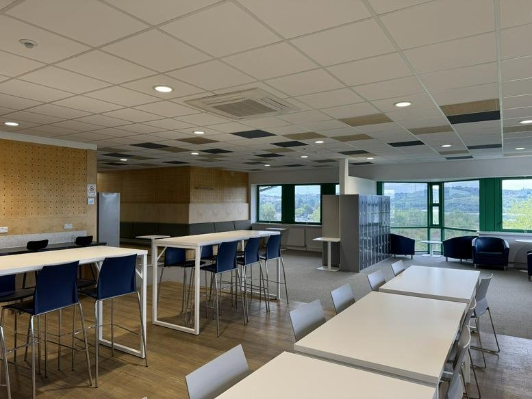 Bright communal break area with high white tables and blue bar stools.