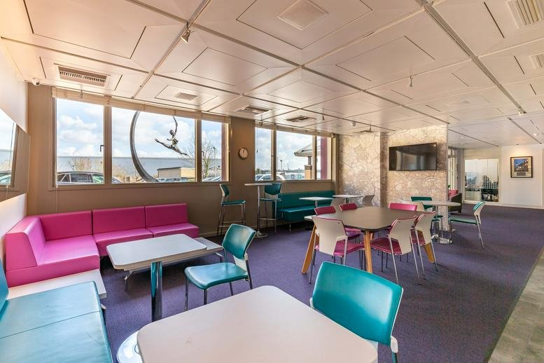 Colorful breakout area at Theobald Street, Hertfordshire, Borehamwood with pink sofas and teal chairs.