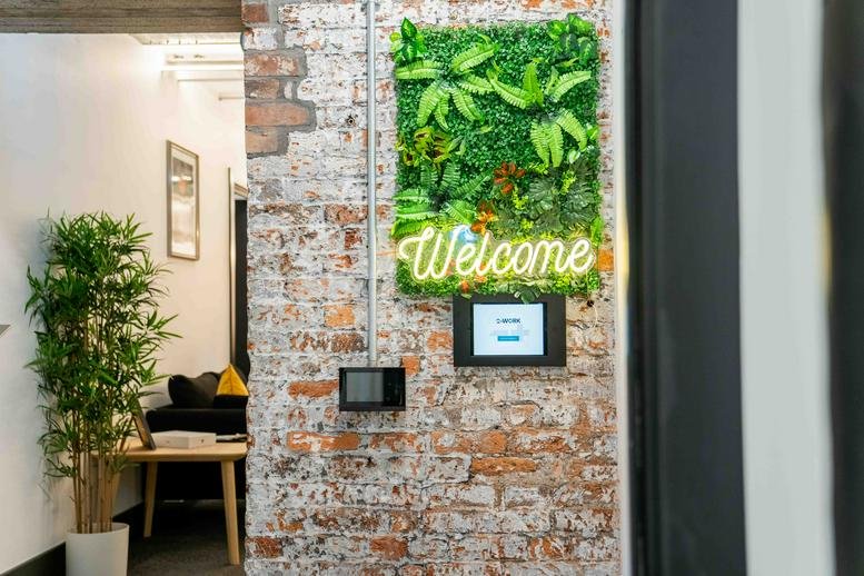 Reception area featuring a brick wall with a green plant feature and neon Welcome sign.