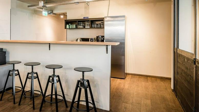 Modern break area at Torstraße 177 with a white breakfast bar, industrial stools, and stainless steel fridge.