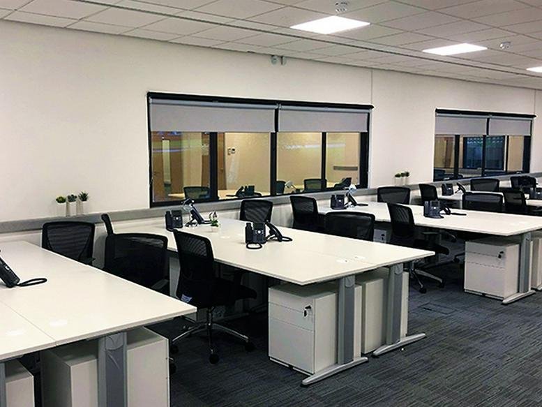Open-plan workspace with white desks, black chairs, and large internal windows.