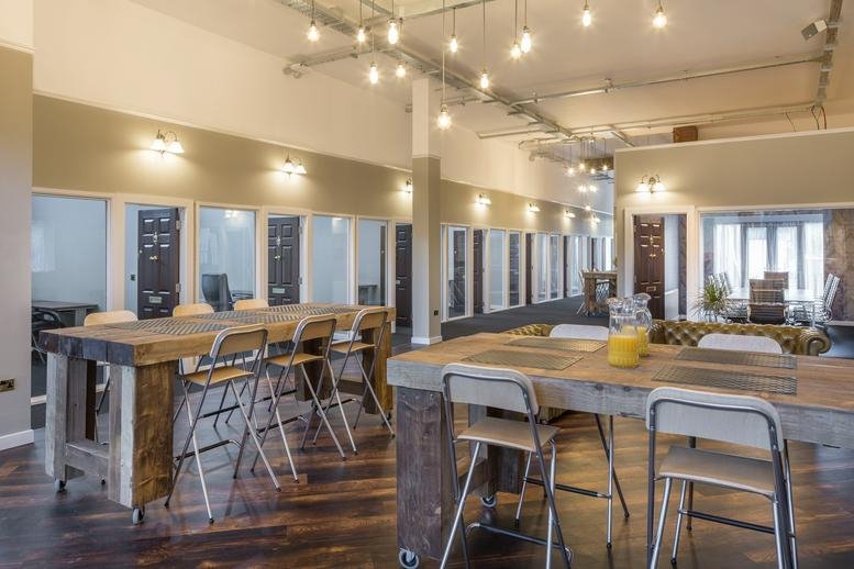Spacious communal coworking area at Trinity House, Newby Rd, Stockport with wooden tables and warm pendant lighting.