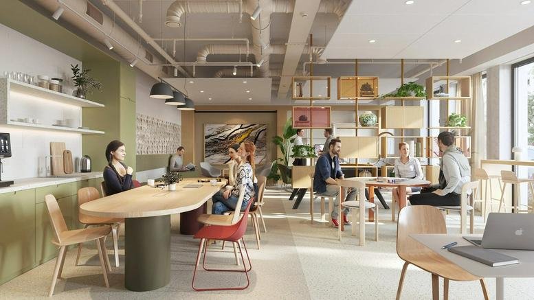 Busy coworking space with people working at long wooden tables and various seating options.