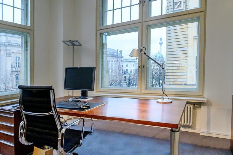 Bright private office featuring a wooden desk, black leather chair, and large windows with city views.