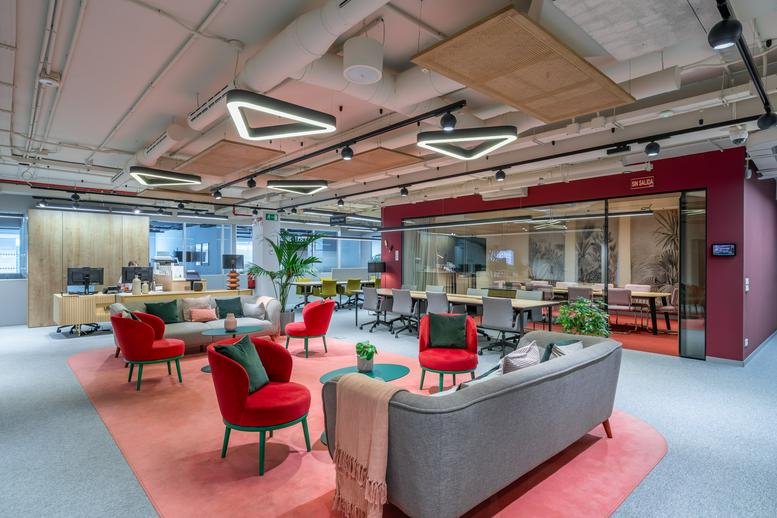 Colorful communal lounge at Utopicus Castellana with red armchairs and triangular ceiling lights.