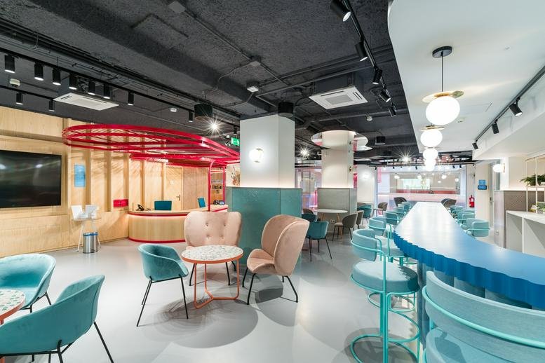 Spacious communal lounge and reception area at Utopicus Paseo de la Habana with modern teal and coral furniture.