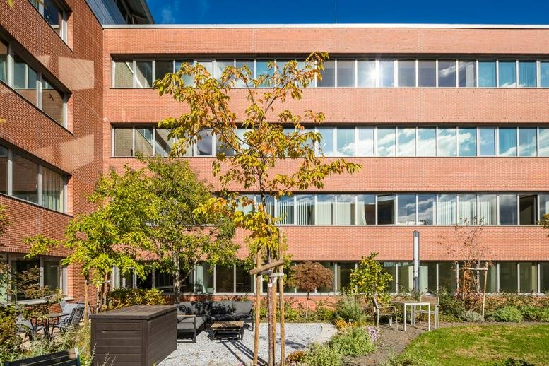 Modern red brick exterior of the Váci str 1-3 building featuring a leafy courtyard garden area.