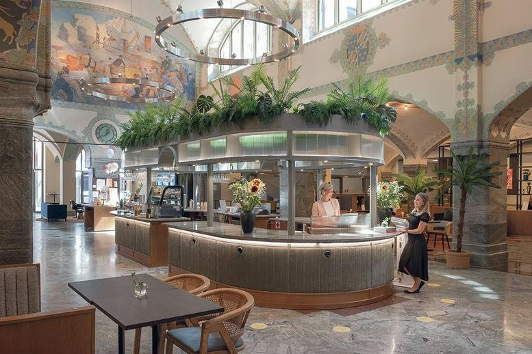 Grand lobby area with a circular service counter, high ceilings, and lush greenery.