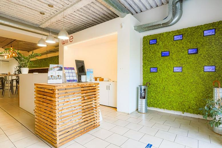 Bright reception area featuring a wooden slat desk and a vibrant green moss wall with digital screens.