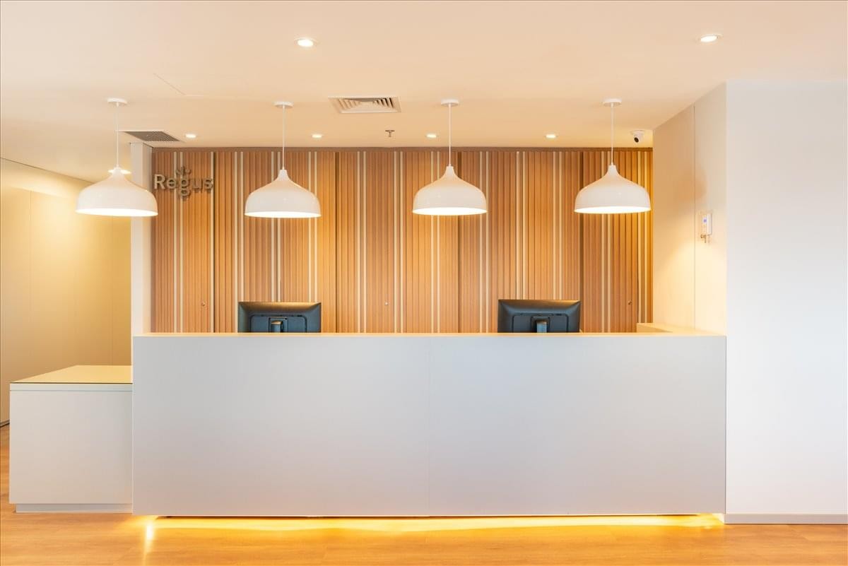 Bright reception area with a minimalist white desk, wooden feature wall, and pendant lighting.