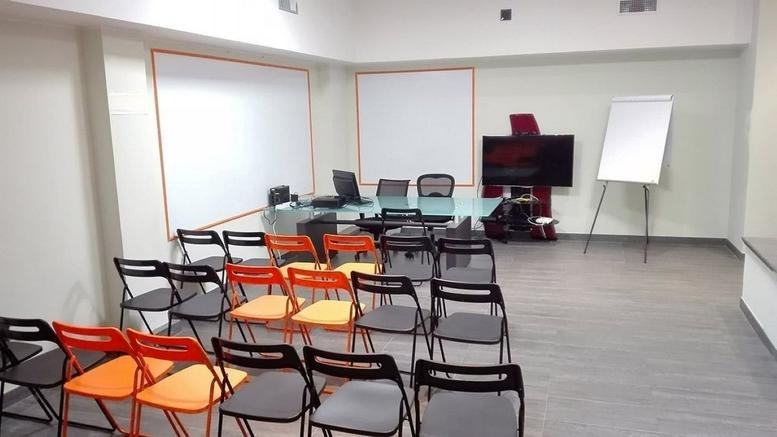 Spacious meeting room at Via Lodovico Montegani, 23, Milan with rows of orange and black chairs and whiteboards.