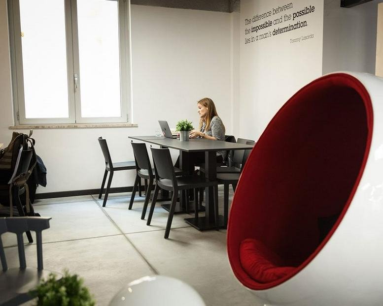 Meeting room with a white and red egg chair, long black table, and natural light at Via Ostiense, 92, Rome, Italy.