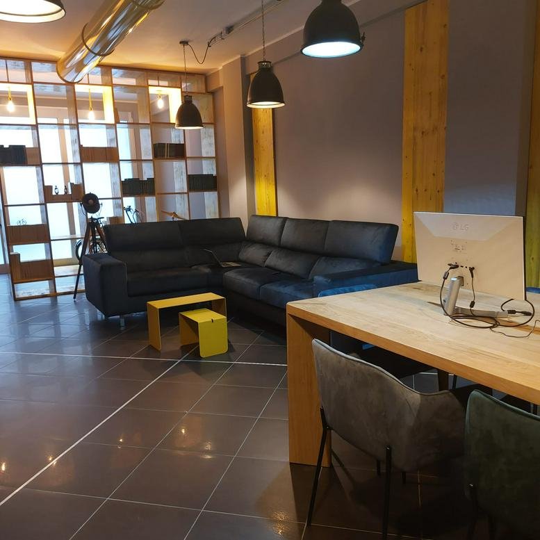 Spacious coworking area at Via Ravenna 107 with a dark leather sectional and wooden communal table.