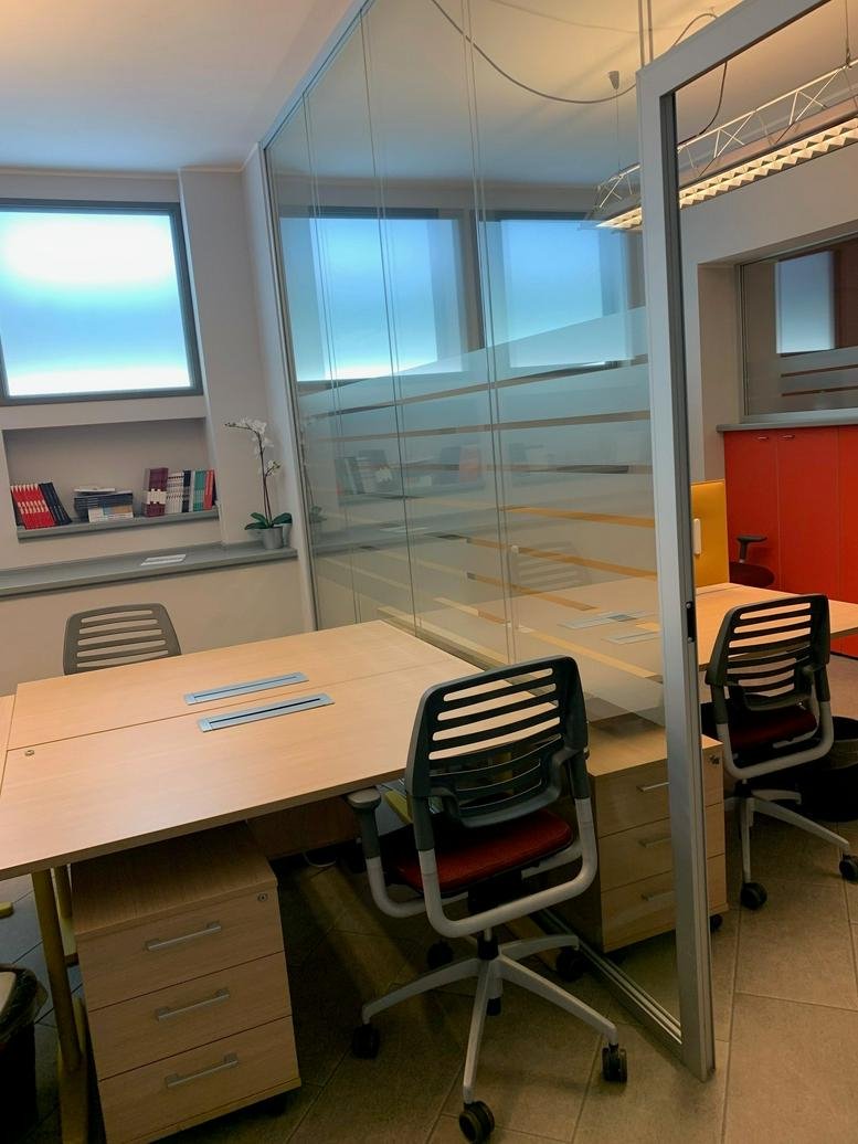 Workspace at Via Salvio Giuliano, 9, Milan featuring modern desks and ergonomic chairs behind glass partitions.