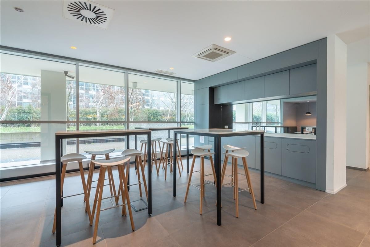 Spacious communal breakout area at Via Milano, 10, Milan, Italy with high tables and floor-to-ceiling windows.