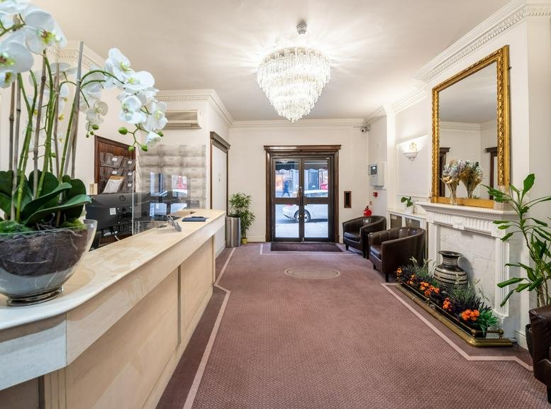 Bright building entrance lobby with a large gold-framed mirror, floral arrangements, and fireplace.