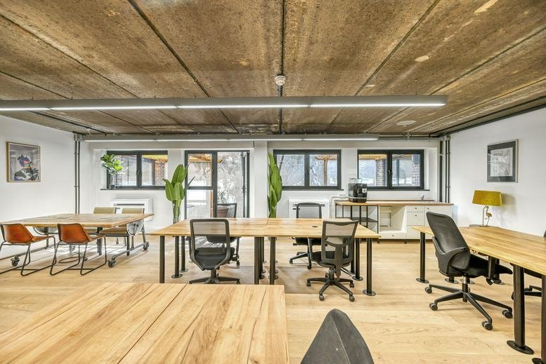 Spacious open-plan workspace at Victoria Park Square with wooden desks, plants, and industrial concrete ceilings.
