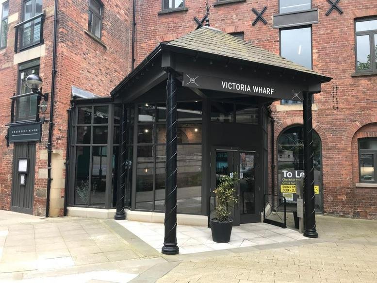 Exterior entrance of Victoria Wharf featuring a black glass-enclosed canopy and brick facade.